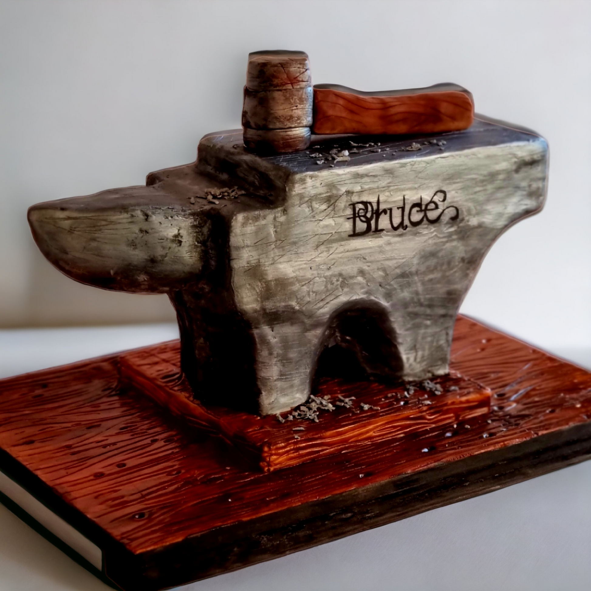 Custom anvil-themed cake with a realistic metallic finish, wooden mallet decoration, and personalized engraving reading 'Bruce.' Perfect for blacksmith-inspired celebrations, custom milestone cakes, and unique themed desserts."