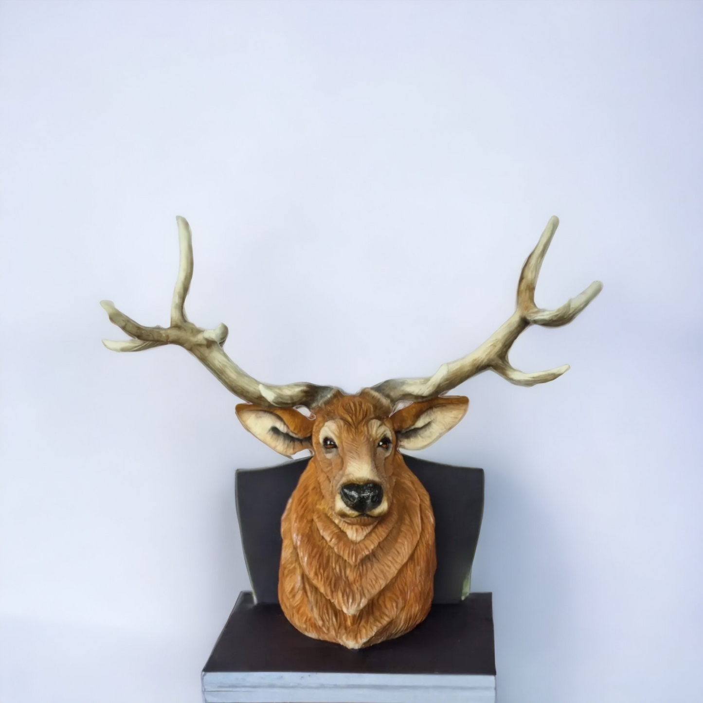 "Realistic deer head cake with intricate details, including textured fur and large antlers, displayed on a sleek black base against a plain background."