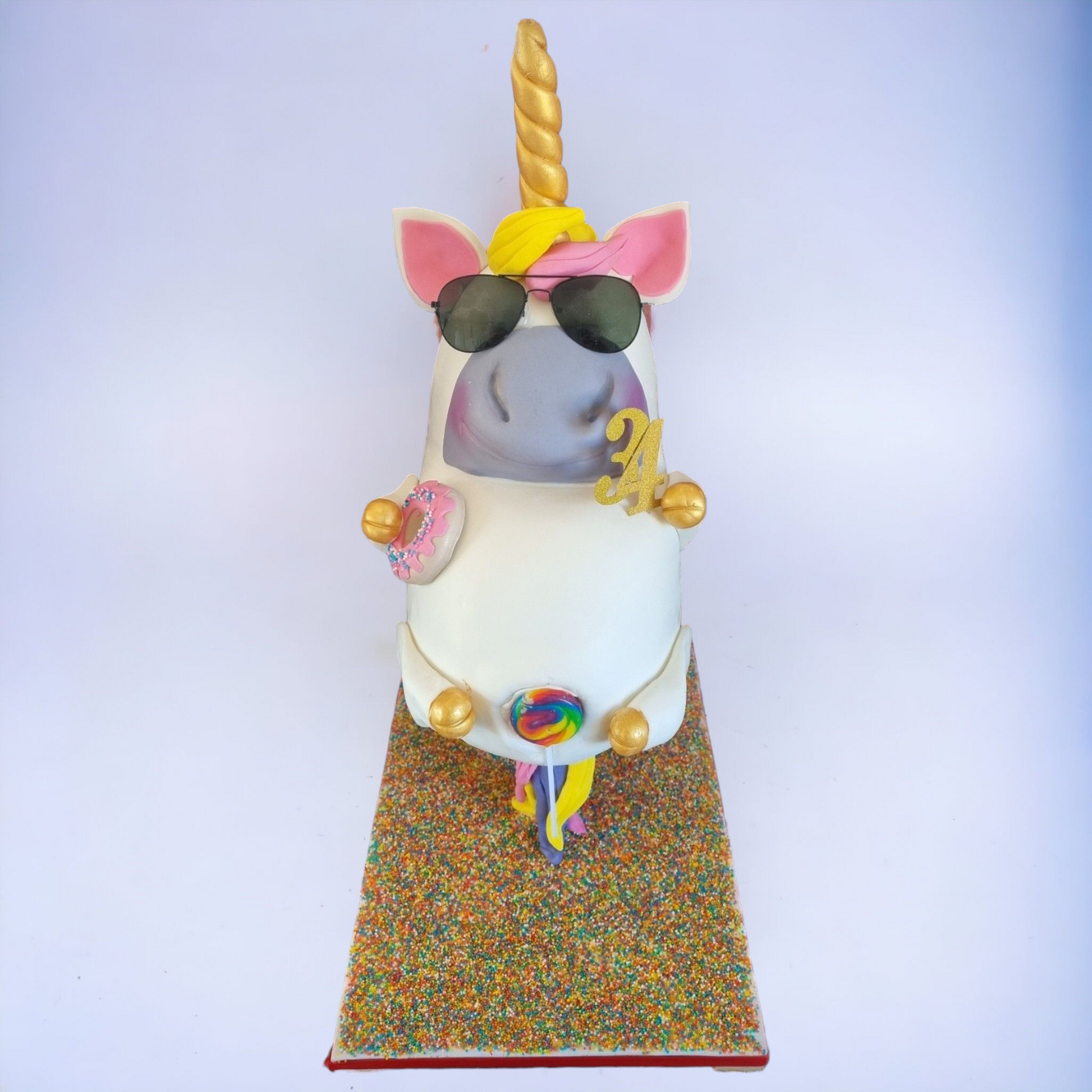 "Fun unicorn cake with whimsical details, including a golden horn, sunglasses, pink ears, and colorful decorations like a lollipop and donut. Perfect for unique birthday cakes and custom 3D cake designs."